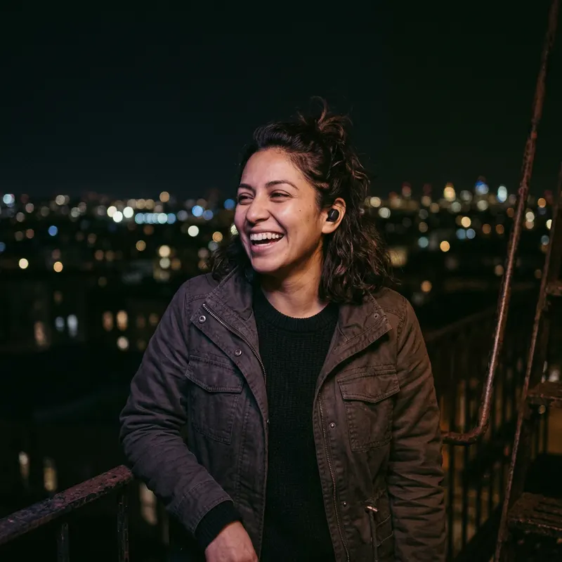 A woman laughing at night, the lights of a city behind her.